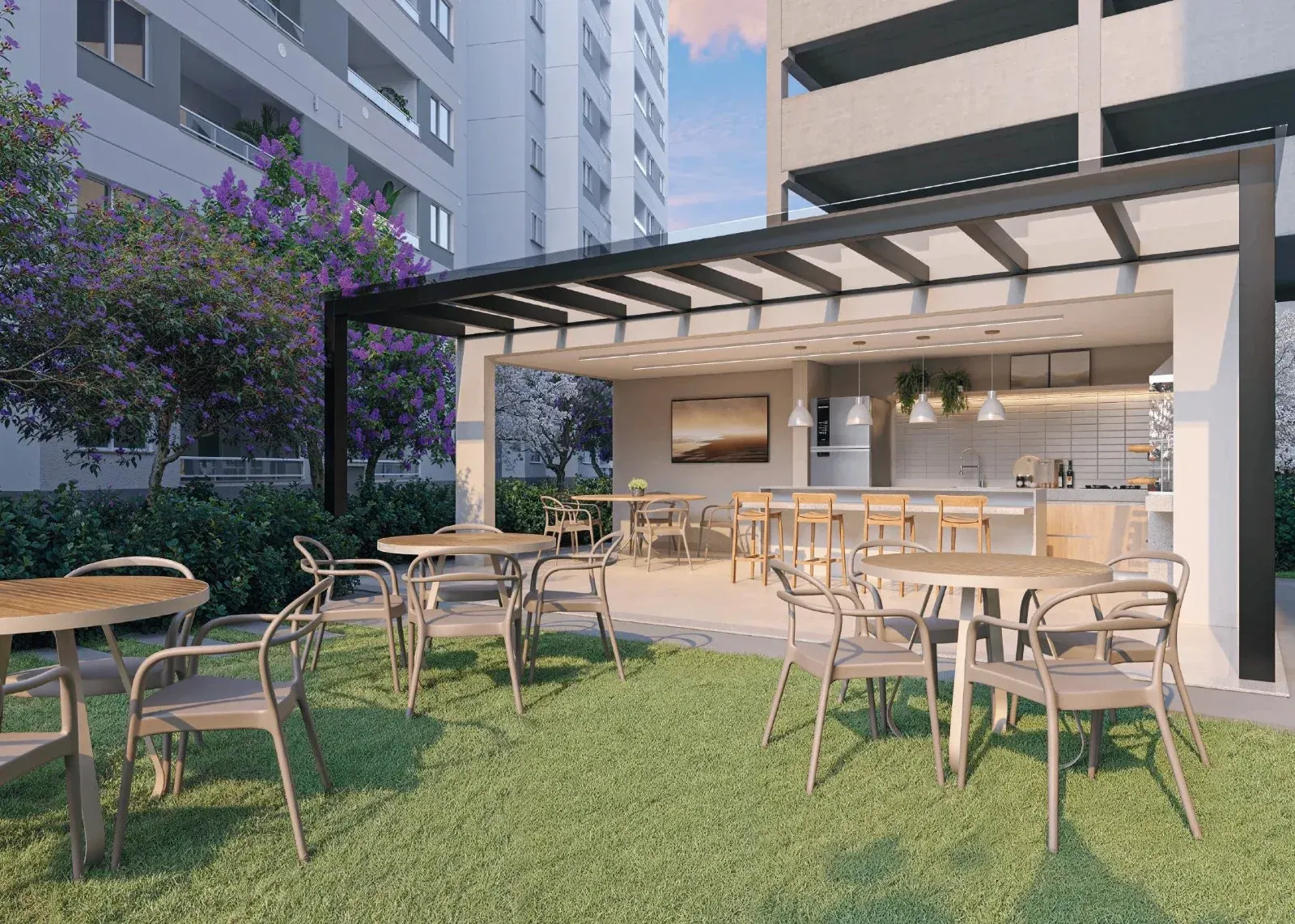 Área gourmet do Sinfonia Santo Amaro by Emccamp: pergolado com churrasqueira, cozinha integrada, mesas ao ar livre sobre o gramado e paisagismo com ipês floridos entre as torres residenciais